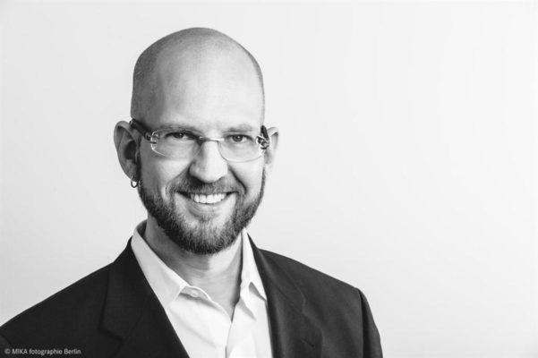 A man with glasses and bald head wearing a suit.