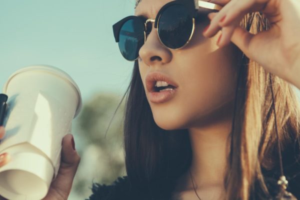 A woman with sunglasses on holding onto a cup of coffee.