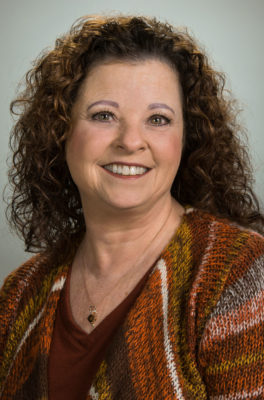 A woman with curly hair and a brown sweater.